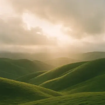 Sunlight breaks through clouds, illuminating a series of lush green rolling hills.