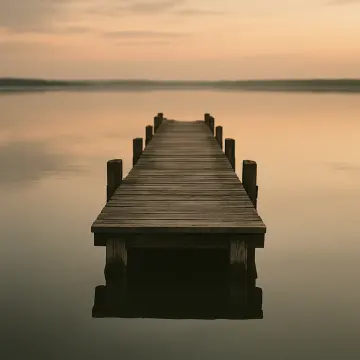 A long wooden pier extends straight into tranquil water under a hazy, orange-toned sky.